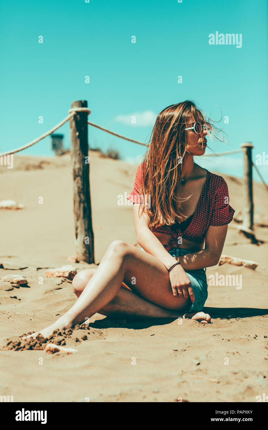 Giovane donna seduta sulla spiaggia sabbiosa Foto Stock