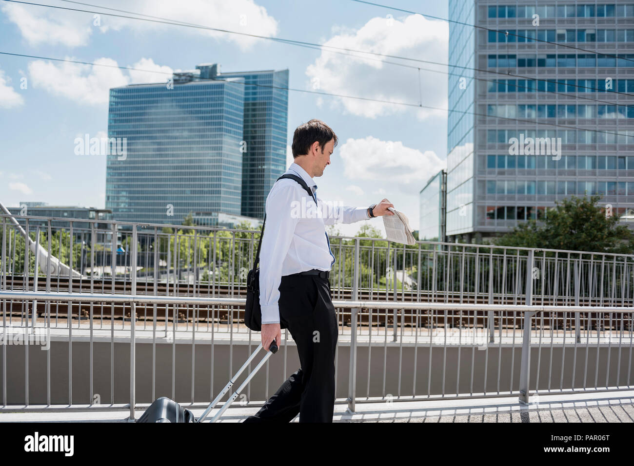 Imprenditore con valigia scorrevole su un ponte controllando il tempo Foto Stock