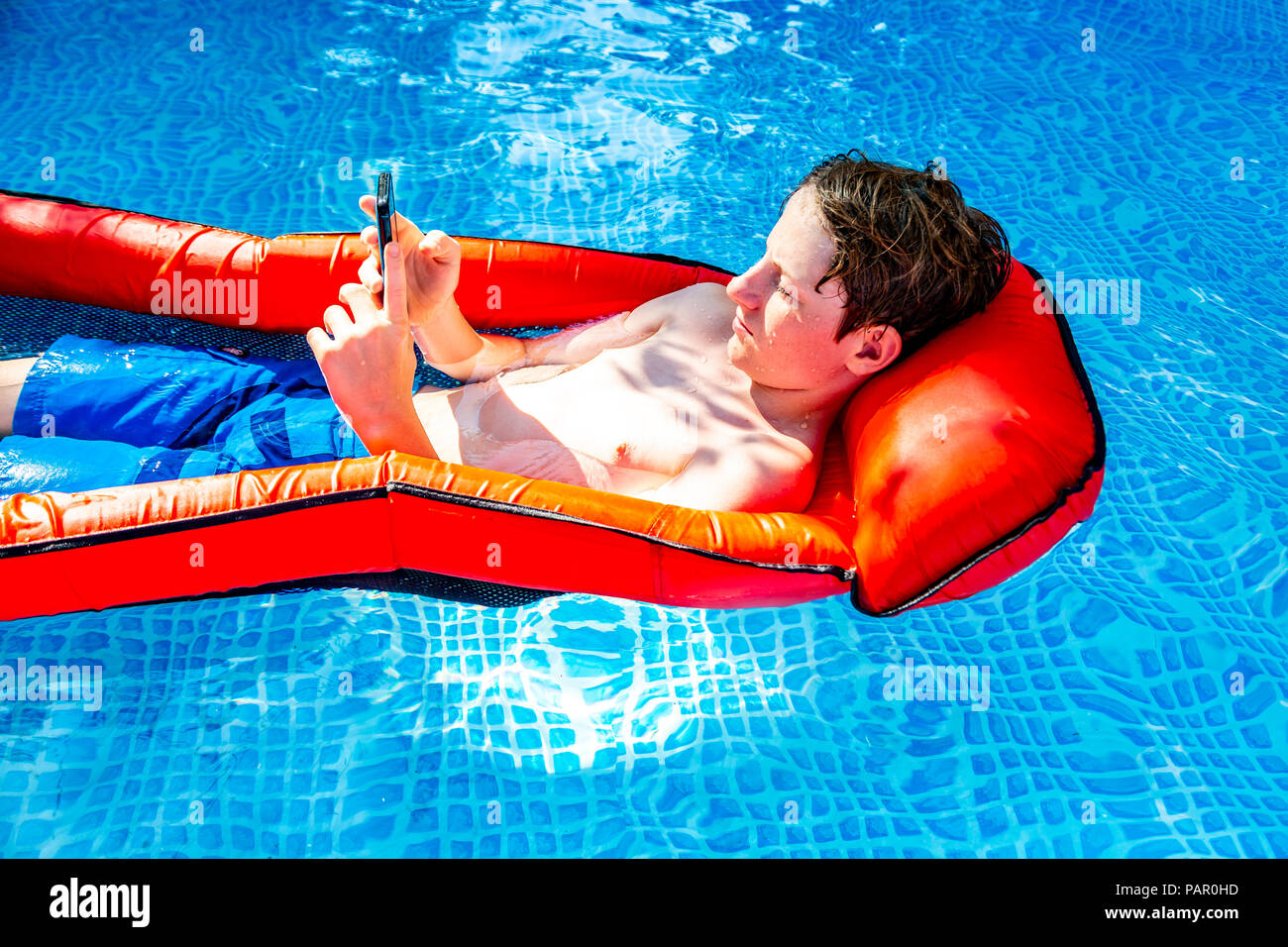 Ragazzo galleggiante sull'acqua in piscina utilizza lo smartphone Foto Stock