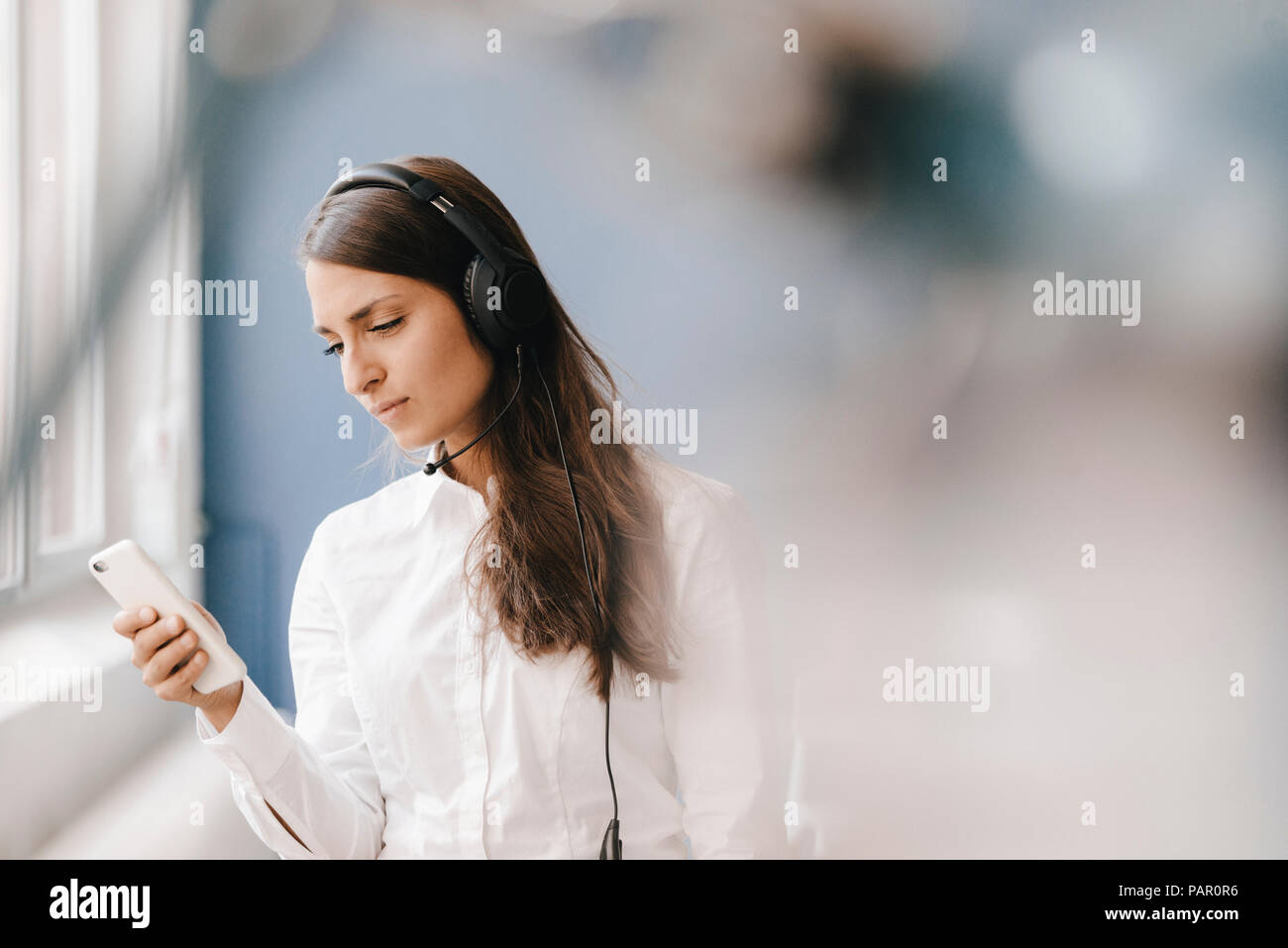 Giovane donna utilizza lo smartphone, indossando le cuffie Foto Stock