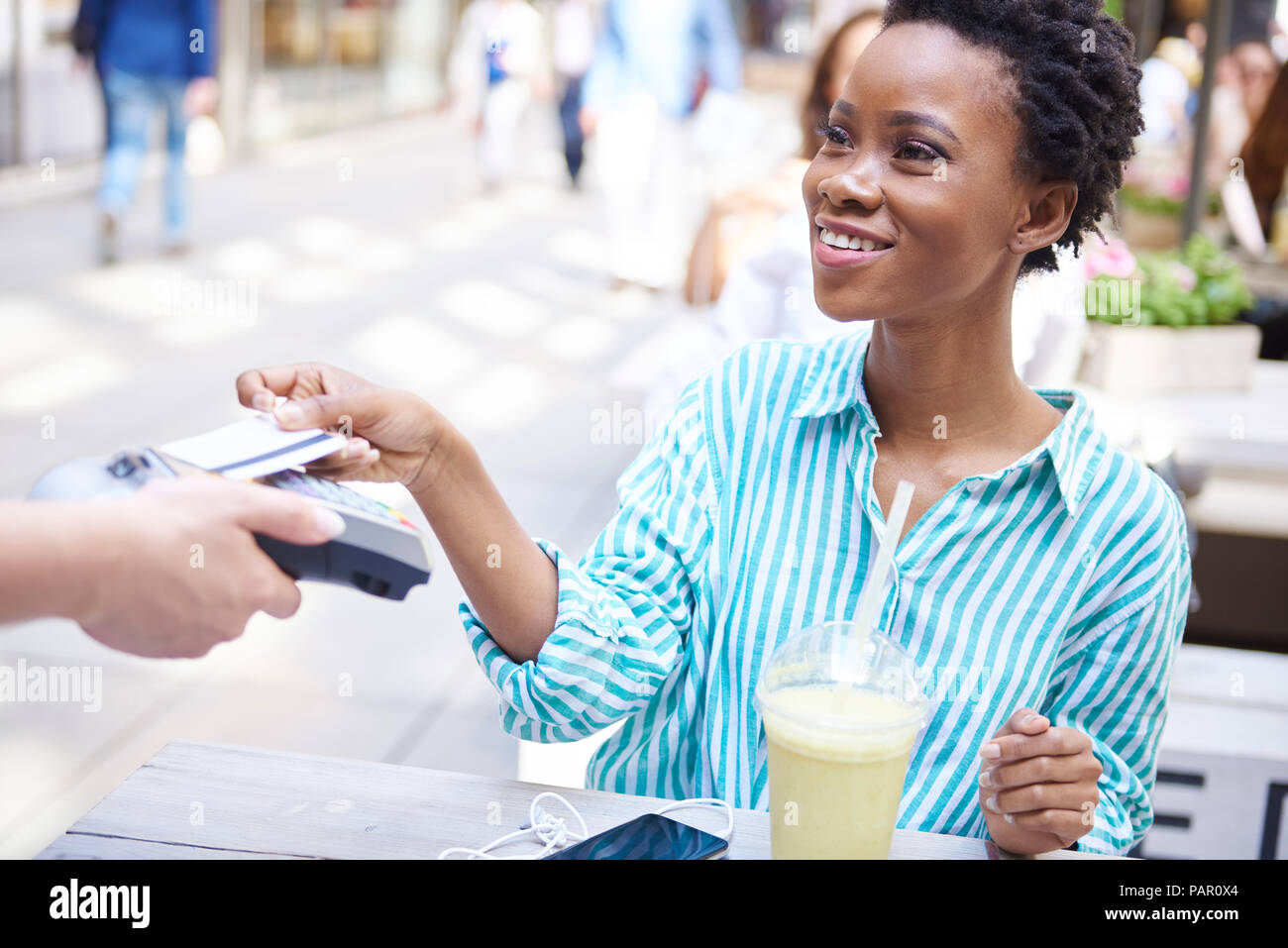 Ritratto di donna sorridente di pagare mediante carta di credito presso pavement cafe Foto Stock