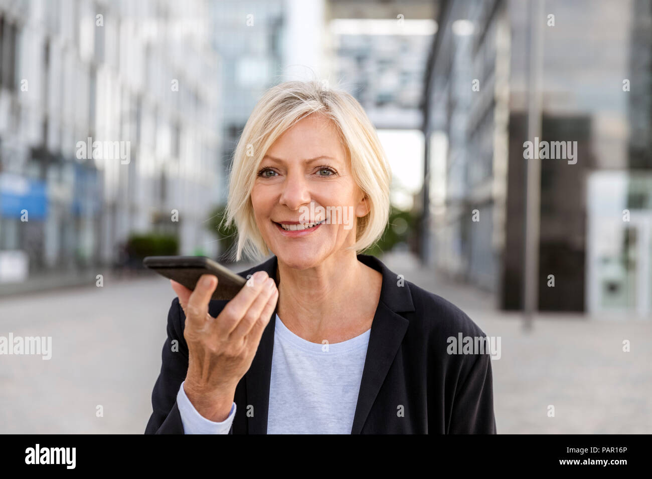Ritratto di sorridere senior imprenditrice tramite telefono cellulare all'aperto Foto Stock