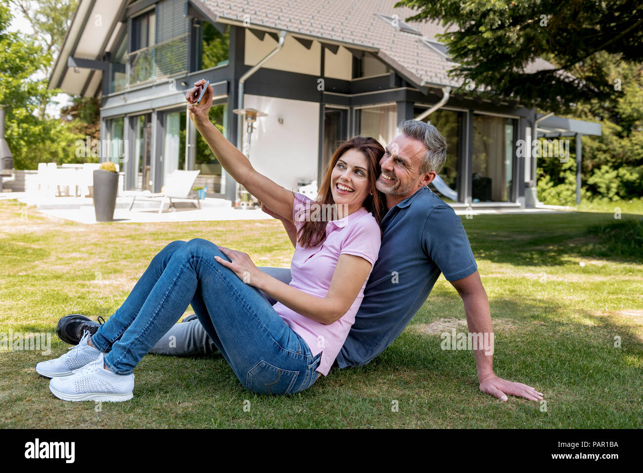 Felice coppia seduta nel giardino della loro casa prendendo un selfie Foto Stock
