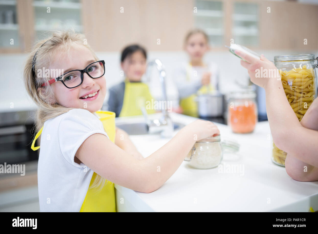 Ritratto di sorridere schoolgirl con classmtes nella classe di cucina Foto Stock