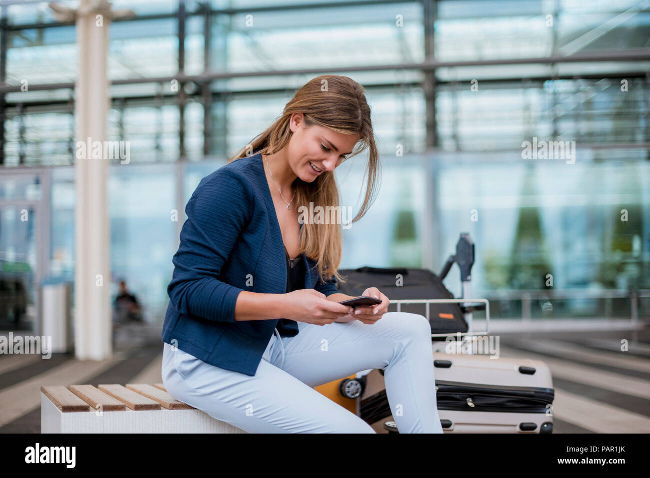 Sorridente giovane imprenditrice seduti all'aperto con un telefono cellulare e la valigia Foto Stock