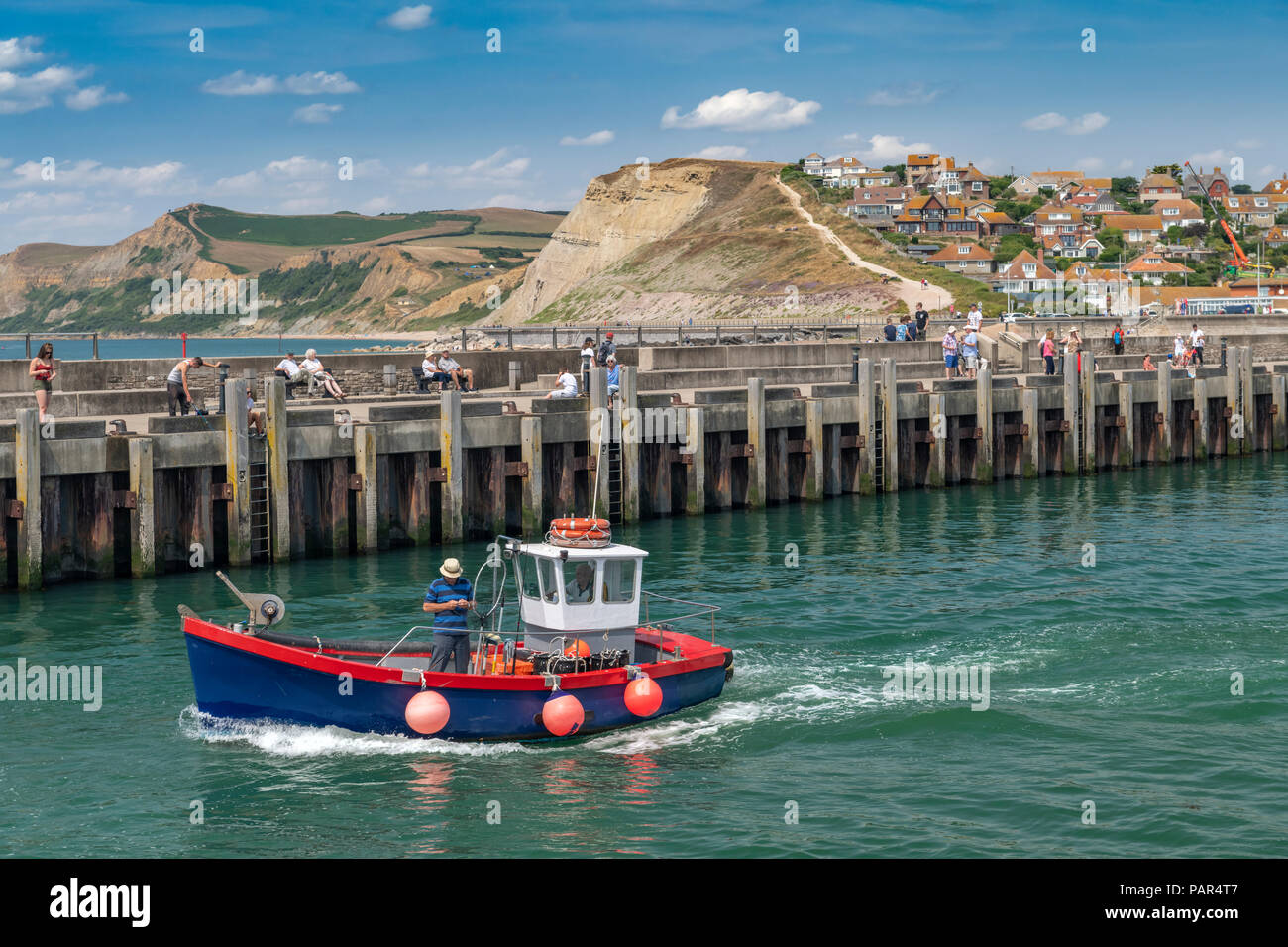 Una piccola barca da pesca lascia il pittoresco porto di West Bay nel Dorset, reso famoso come il luogo per la serie televisiva "Broadchurch'. Foto Stock