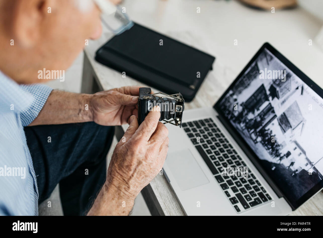 Senior Uomo con laptop e tenendo la sua vecchia foto fotocamera, schermo con vecchie foto Foto Stock