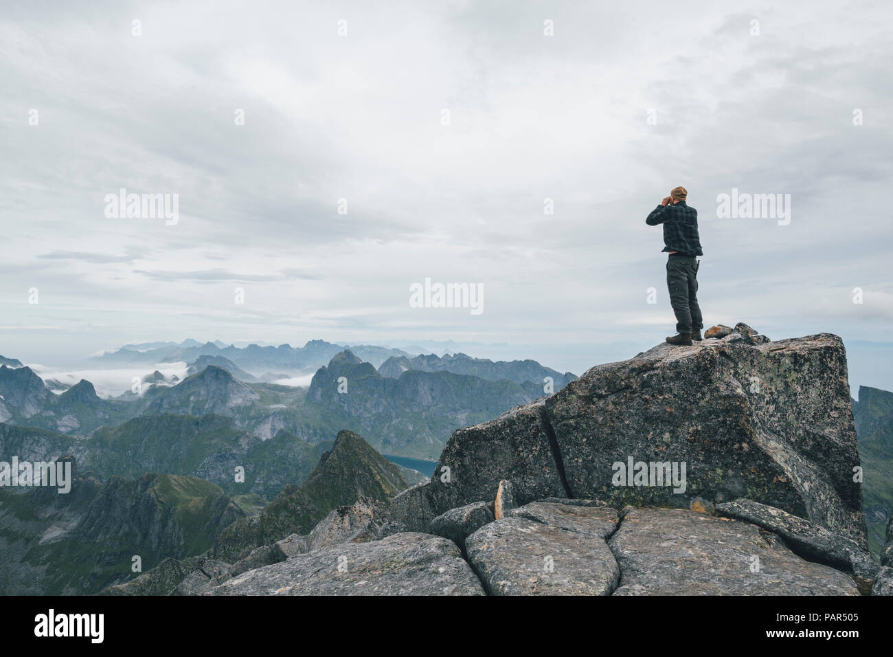 Norvegia Lofoten, Moskenesoy, giovane uomo in piedi alla Hermannsdalstinden, guardando sopra Kjerkefjord Foto Stock