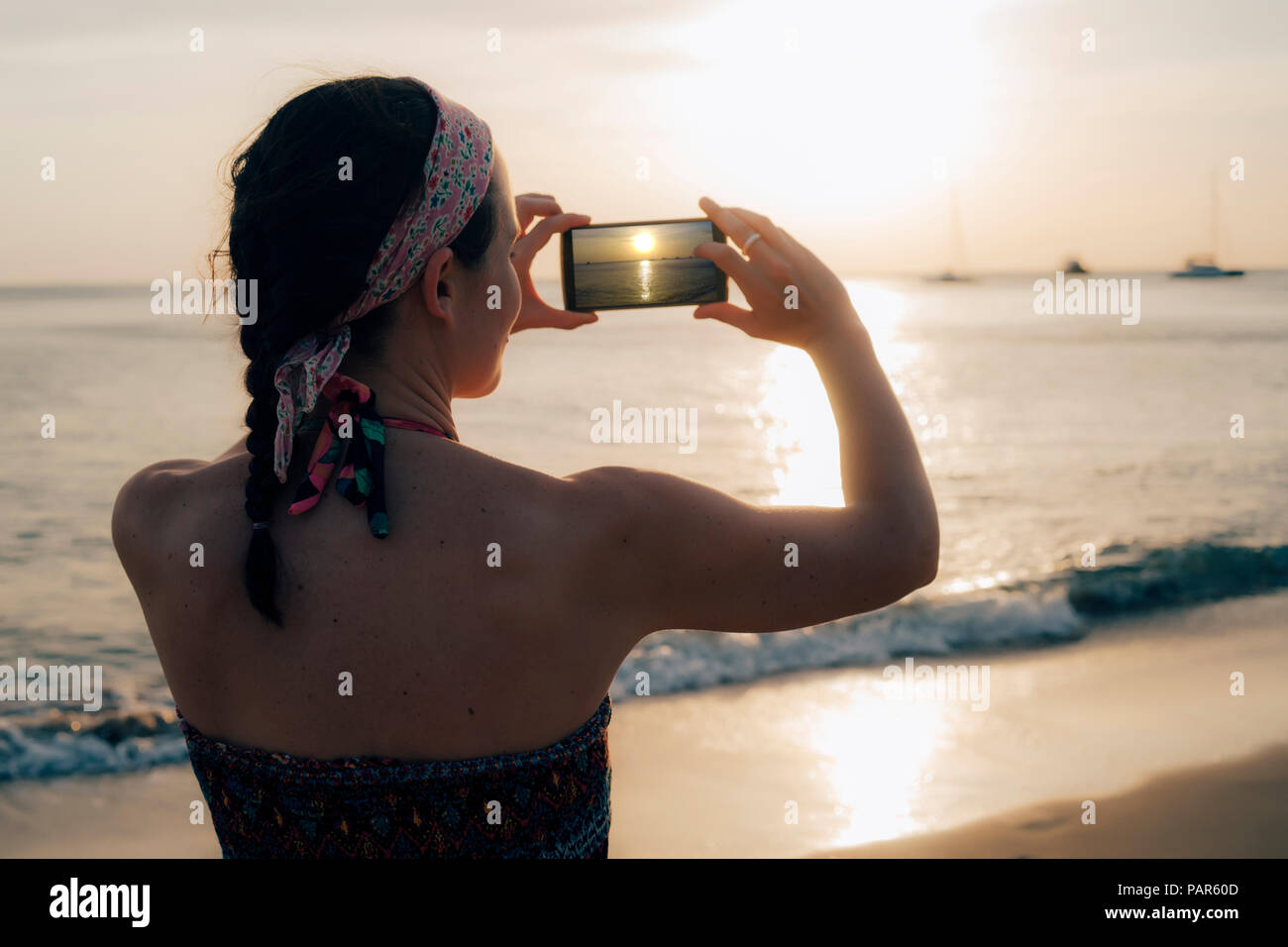 Thailandia Koh Lanta, donna sulla spiaggia prendendo foto con il telefono cellulare al tramonto Foto Stock