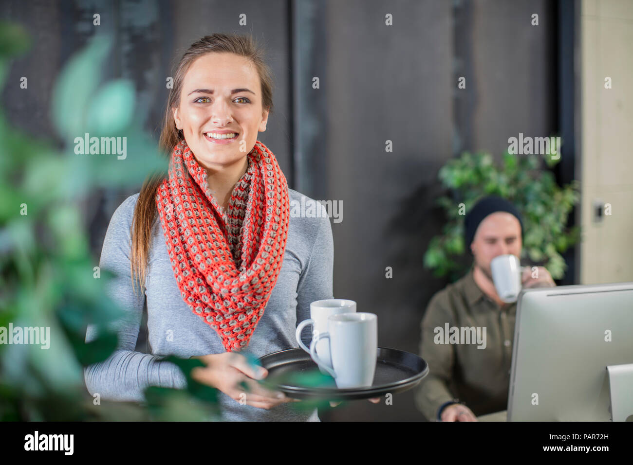 Sorridente giovane donna che serve caffè in ufficio Foto Stock