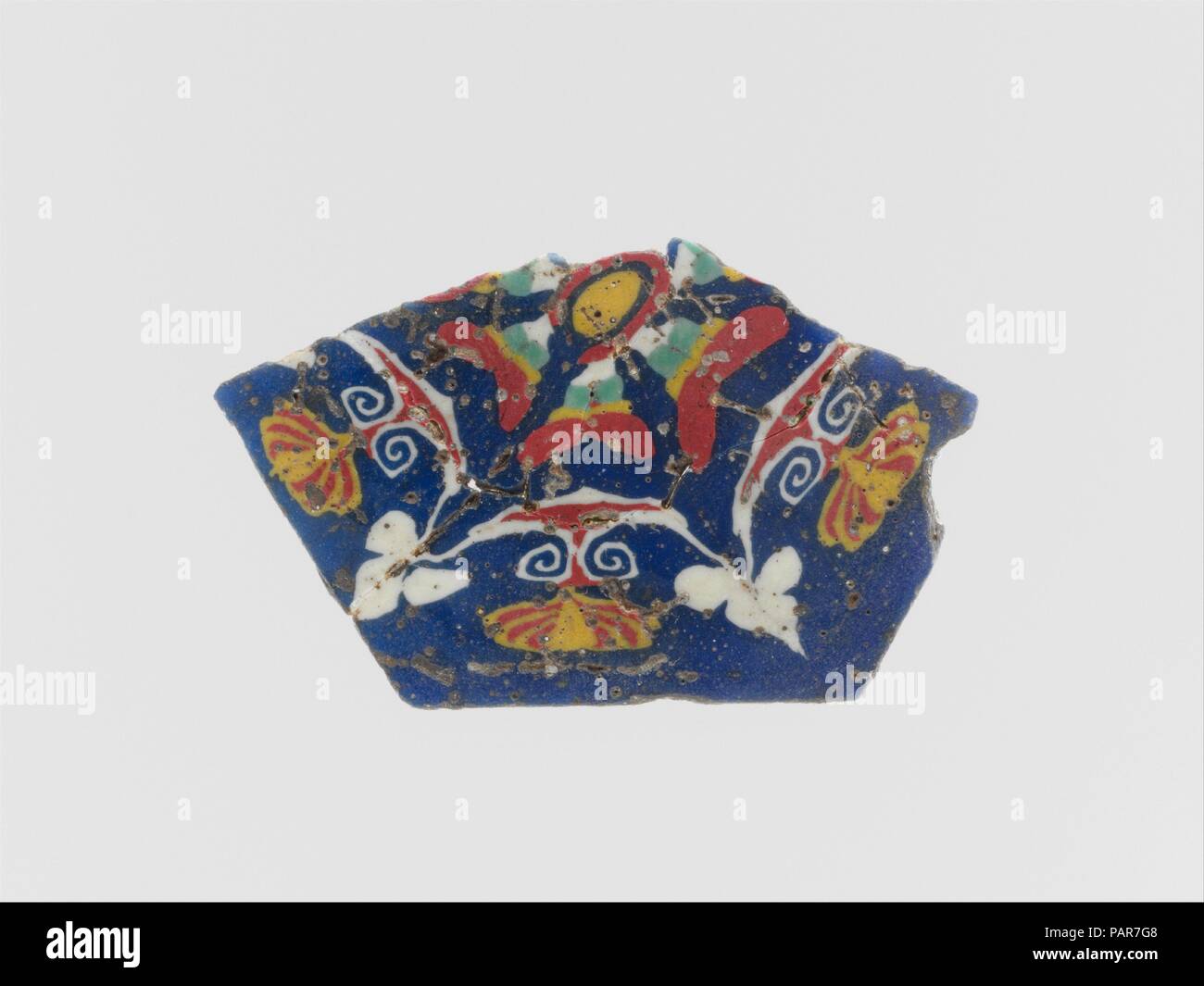 Mosaico di vetro a inserto. Cultura: egiziana, Romano. Dimensioni: Altri: 1 7/16 in. (3.6 cm). Data: fine del I secolo A.C. - inizio del I secolo d.c. Traslucido blu cobalto massa; decorazione in bianco opaco, giallo, rosso e verde grigiastro. Poligonale, piatta, e molto sottile placca. Simmetriche foglia di edera e motivo a palmette disposte intorno a un grande centro di sei-petaled rosetta, con una leggermente compressa a palmette con volute a spirale inferiore sui lati di esagono e foglie d'edera in solido bianco in corrispondenza degli angoli. Suddivisi in medio con quasi la metà del motif mancante; superiore e il lato inferiore e il bordo molato e lucidato; Foto Stock