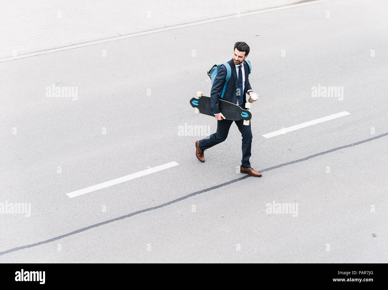 Imprenditore con caffè da asporto e skateboard a camminare sulla strada Foto Stock