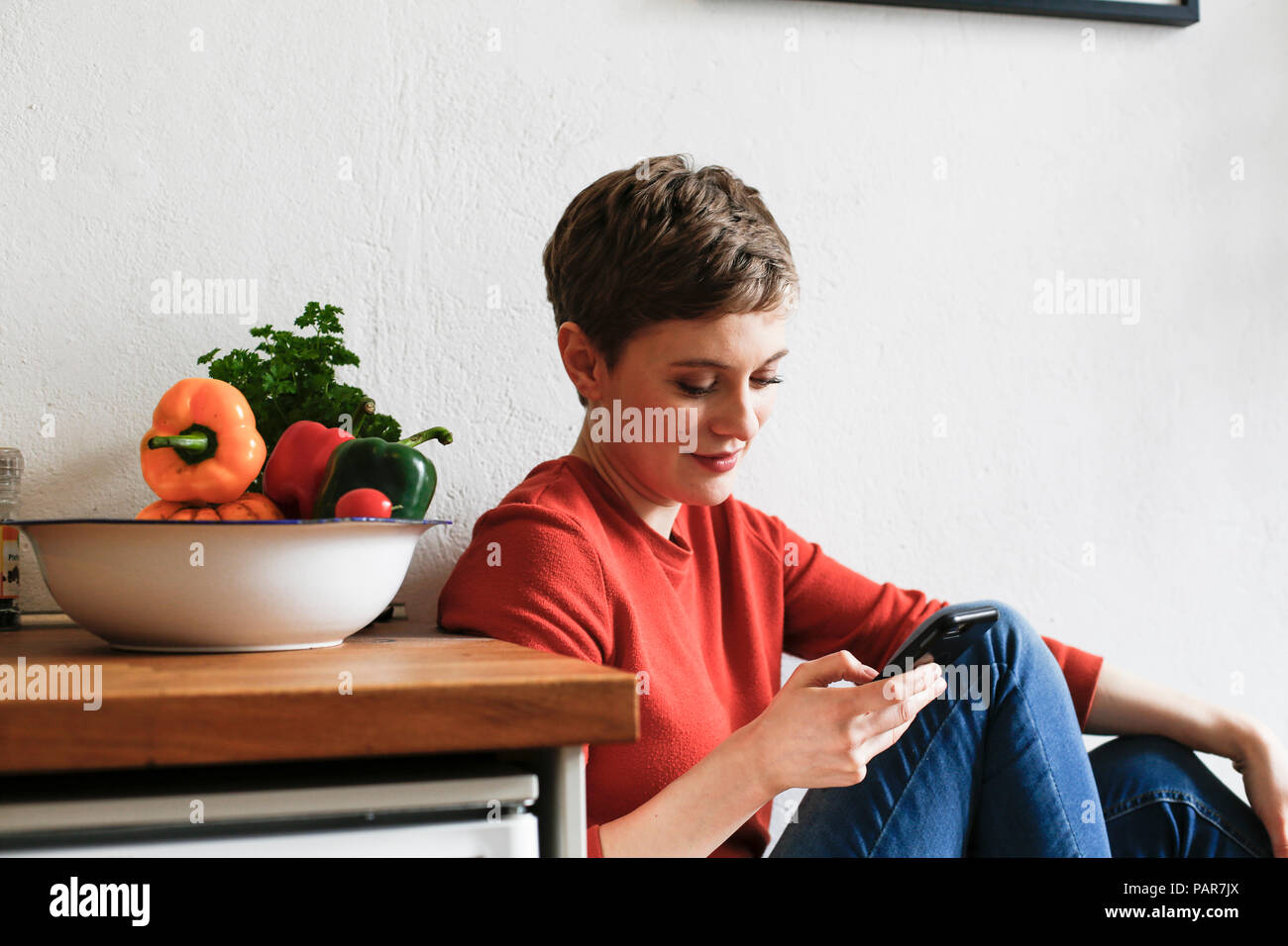 Donna seduta in cucina, controllare i messaggi sullo smartphone Foto Stock
