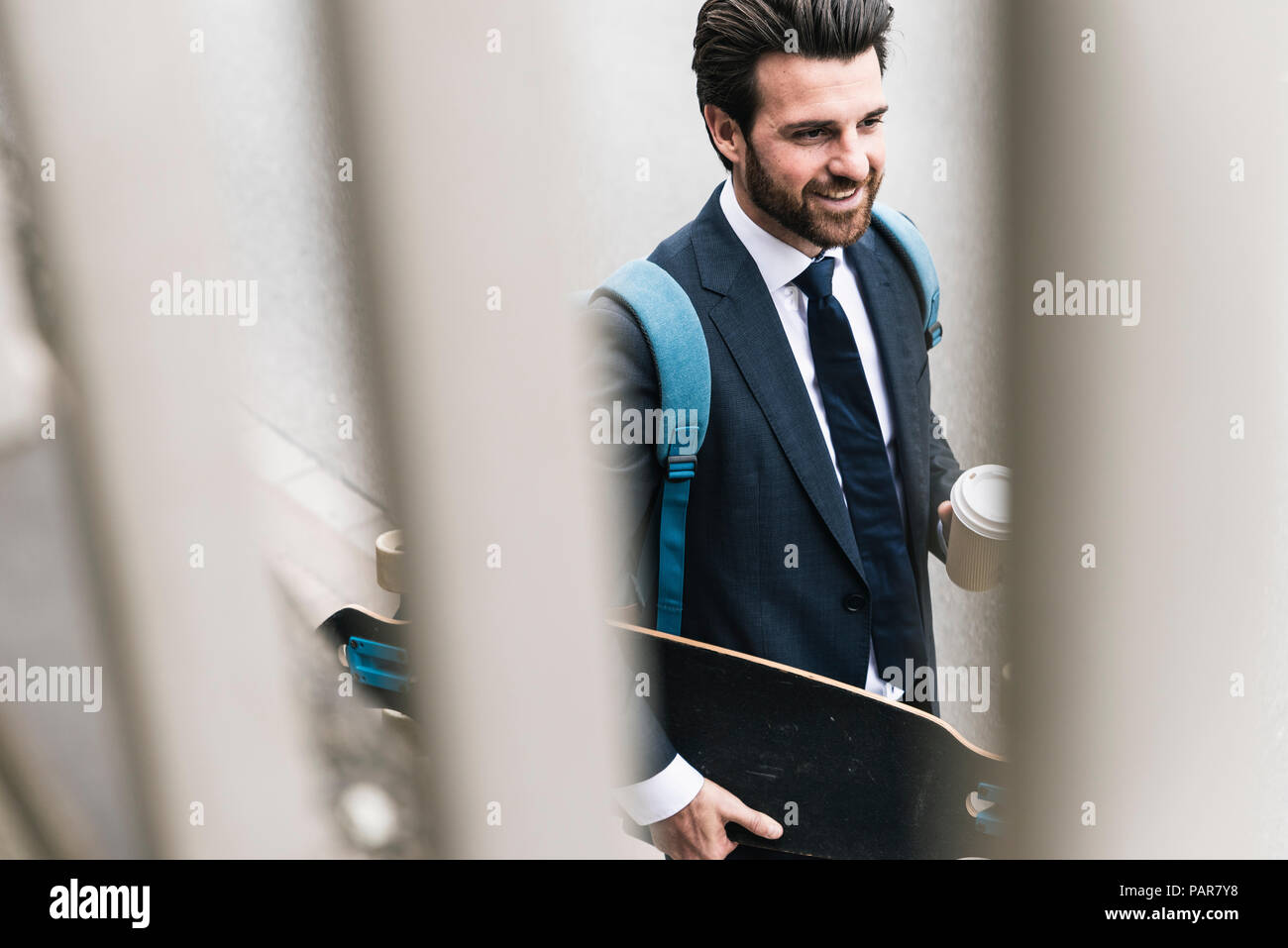 Imprenditore sorridente con il caffè da asporto e skateboard passeggiate all'aperto Foto Stock