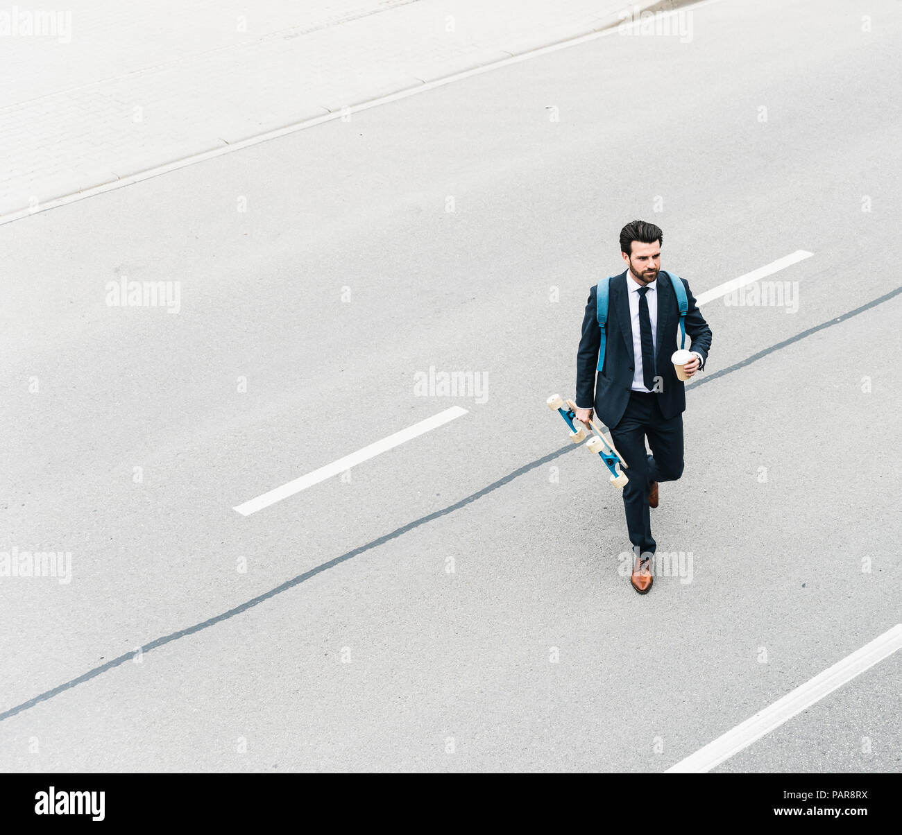 Imprenditore con caffè da asporto e skateboard a camminare sulla strada Foto Stock
