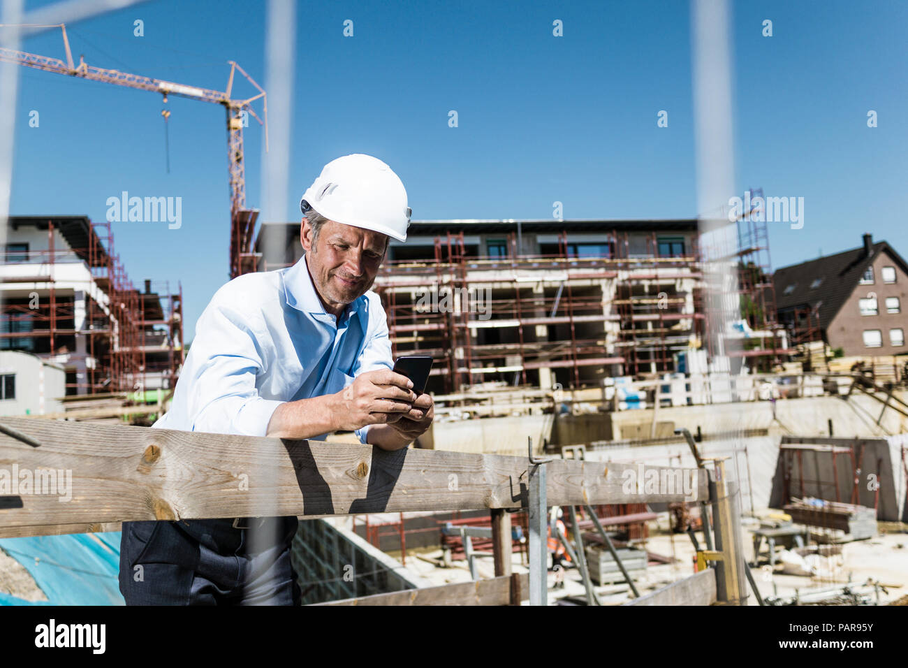 Uomo che indossa elmetto tramite cellulare sul sito in costruzione Foto Stock