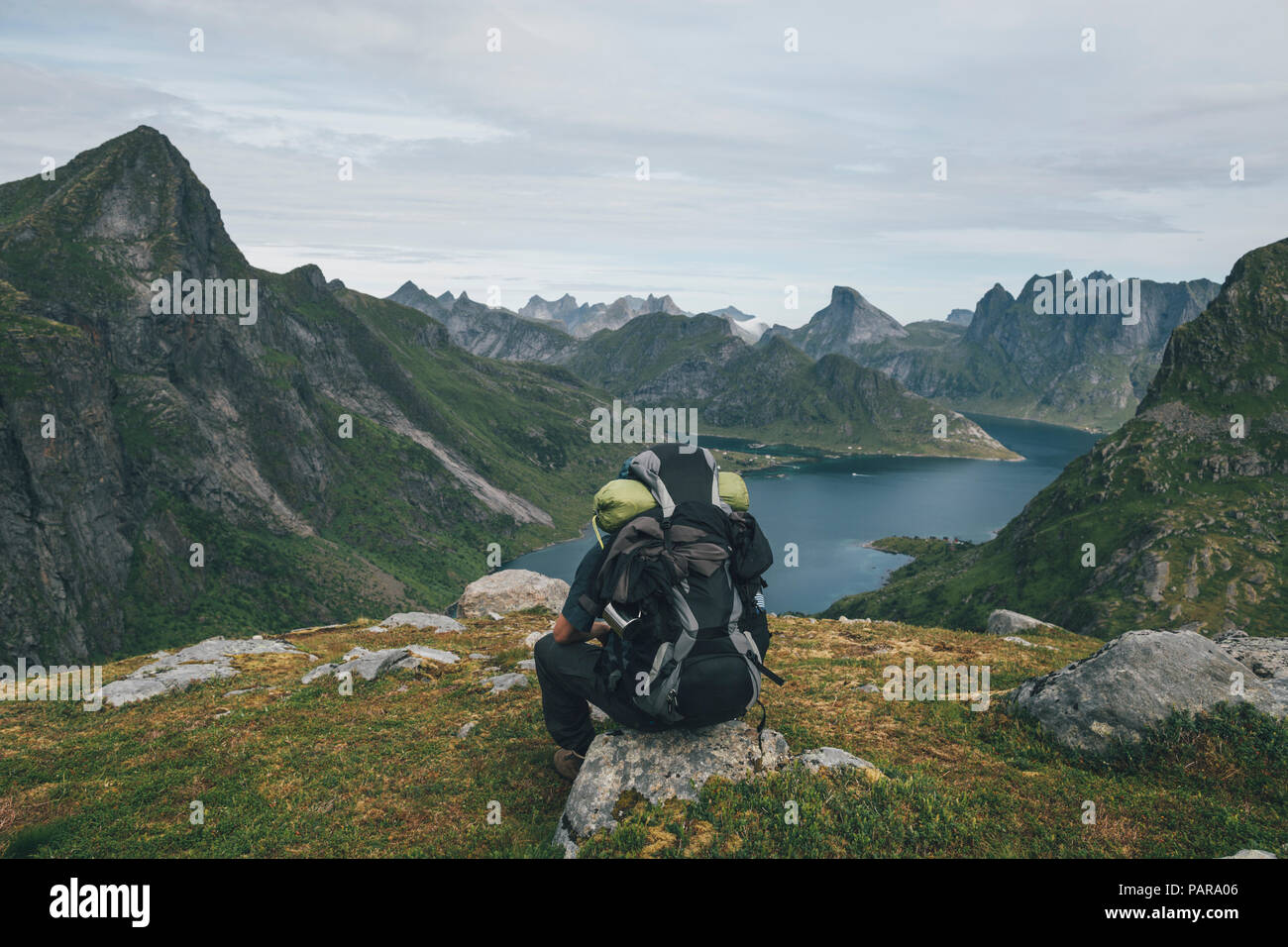 Norvegia Lofoten, Moskenesoy, uomo seduto su una roccia, guardando sopra Kjerkefjord Foto Stock