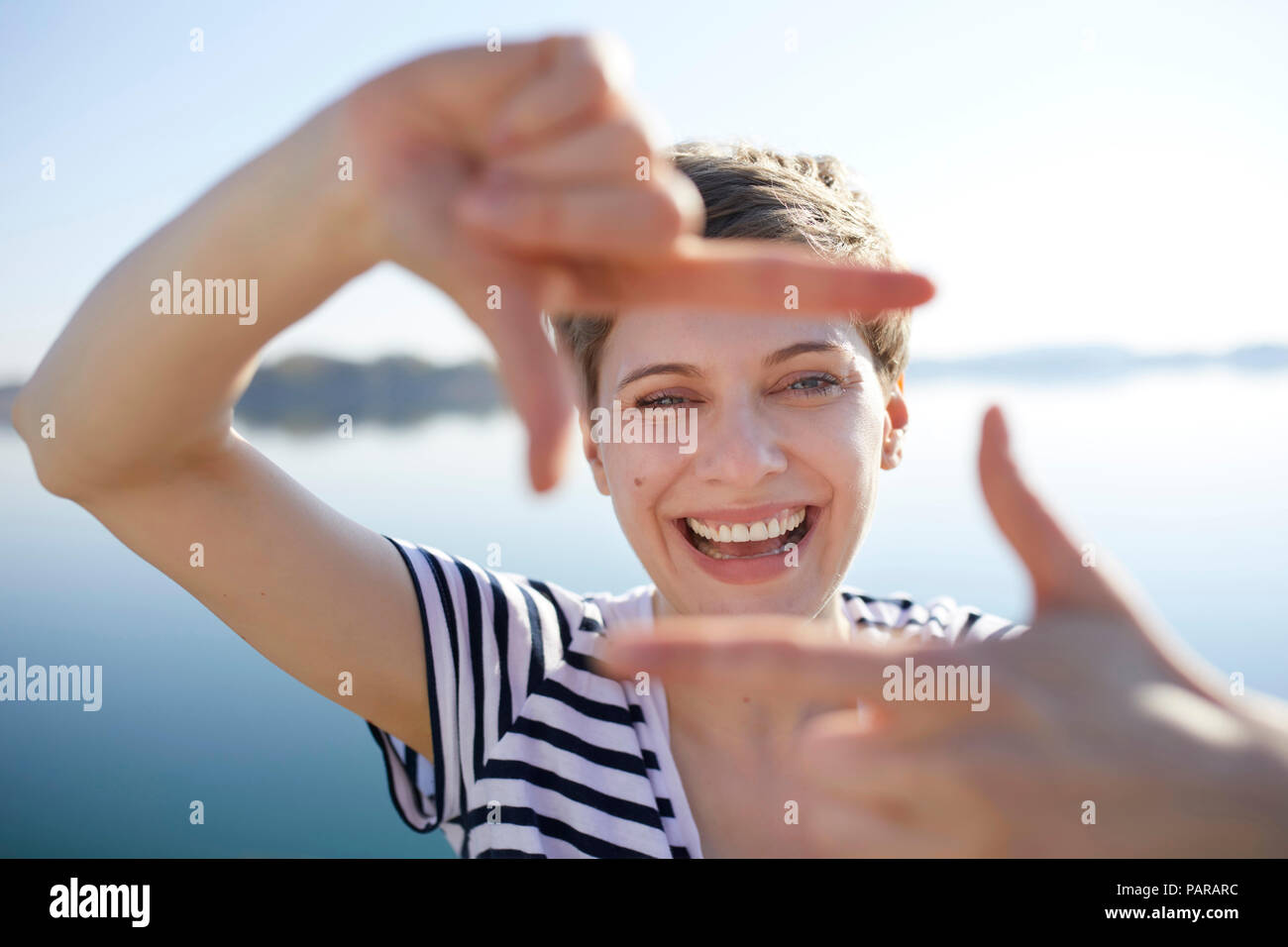 Ritratto di donna ridere di fronte al lago di telaio conformatore con le dita Foto Stock