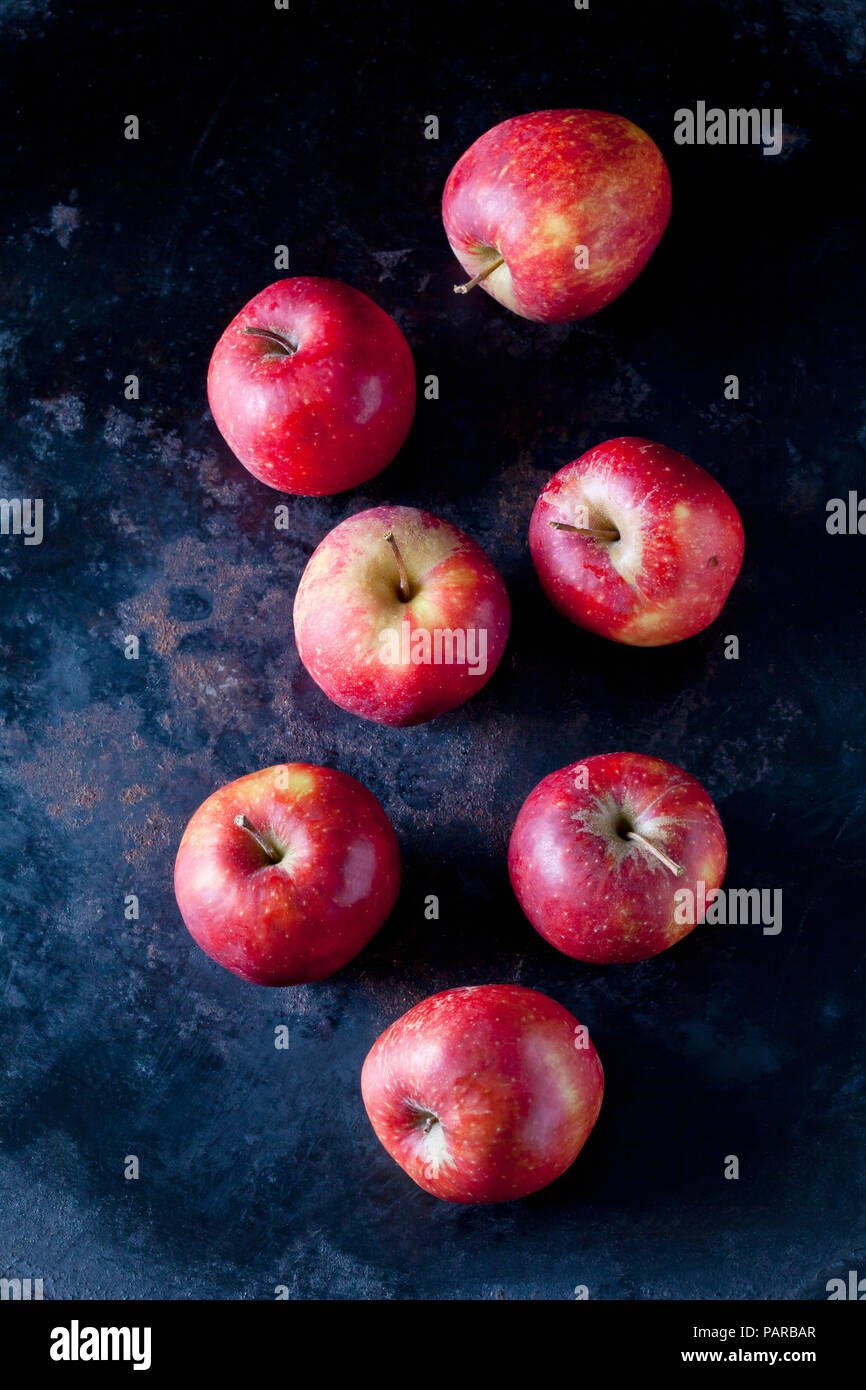 Sette le mele rosse sul terreno scuro Foto Stock