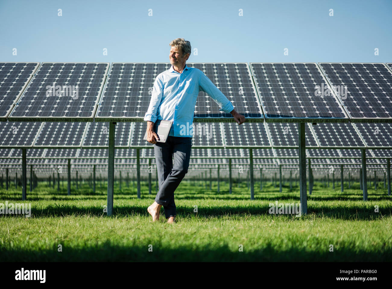 Uomo maturo con il computer portatile a piedi nudi sul prato, impianto solare Foto Stock