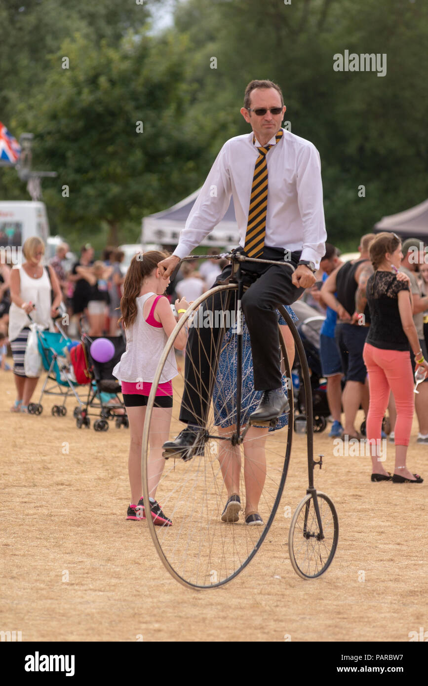 Uomo a cavallo di un penny farthing bicicletta ad un festival di famiglia in estate. Foto Stock