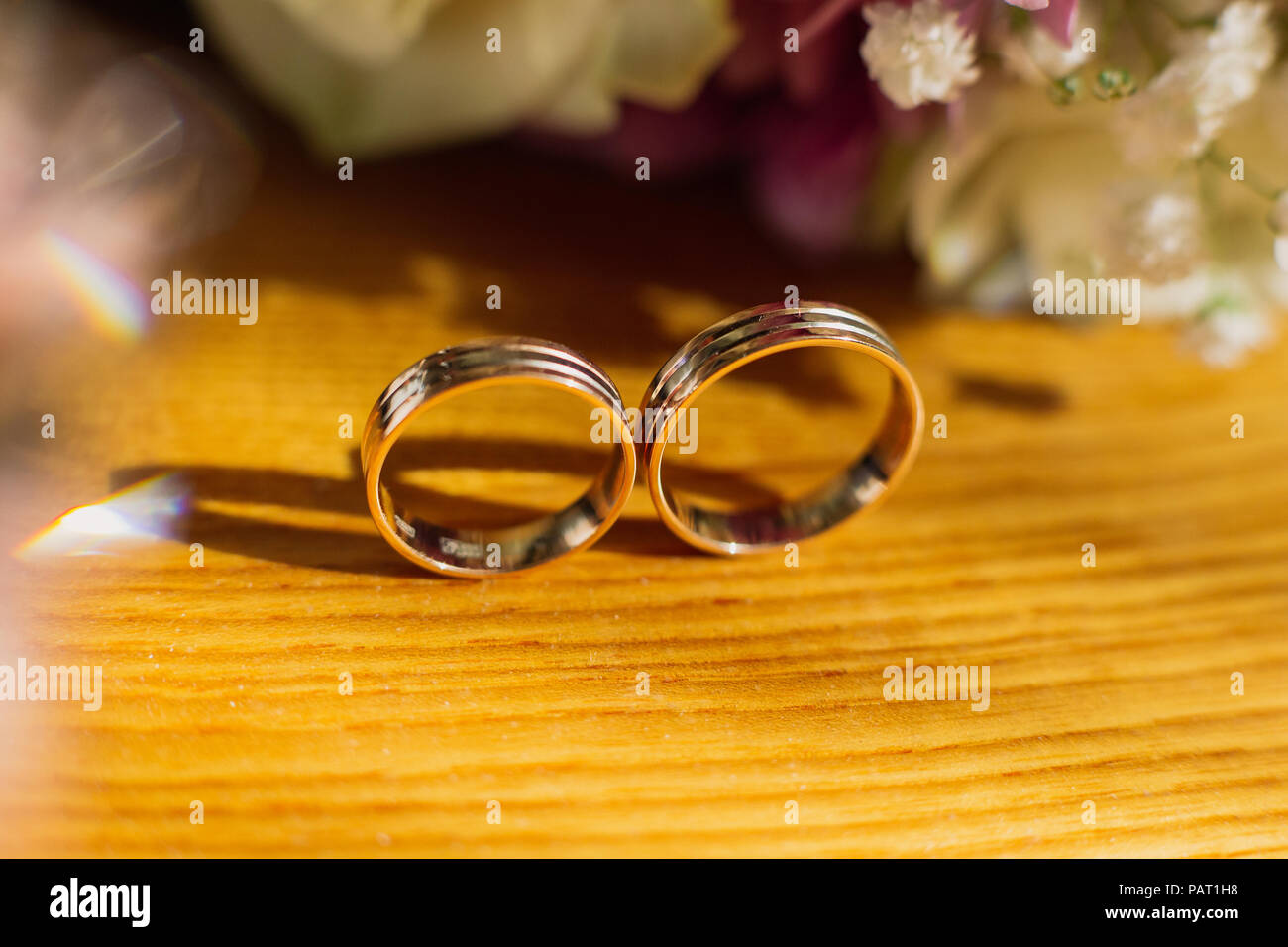Bella tonica foto con gli anelli di nozze giacciono su una superficie di legno contro lo sfondo di un mazzo di fiori. Foto Stock