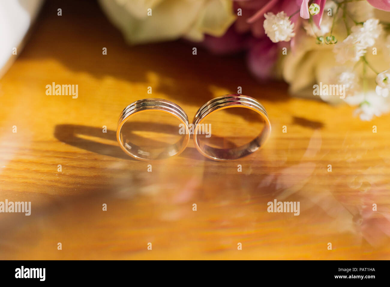 Bella tonica foto con gli anelli di nozze giacciono su una superficie di legno contro lo sfondo di un mazzo di fiori. Foto Stock