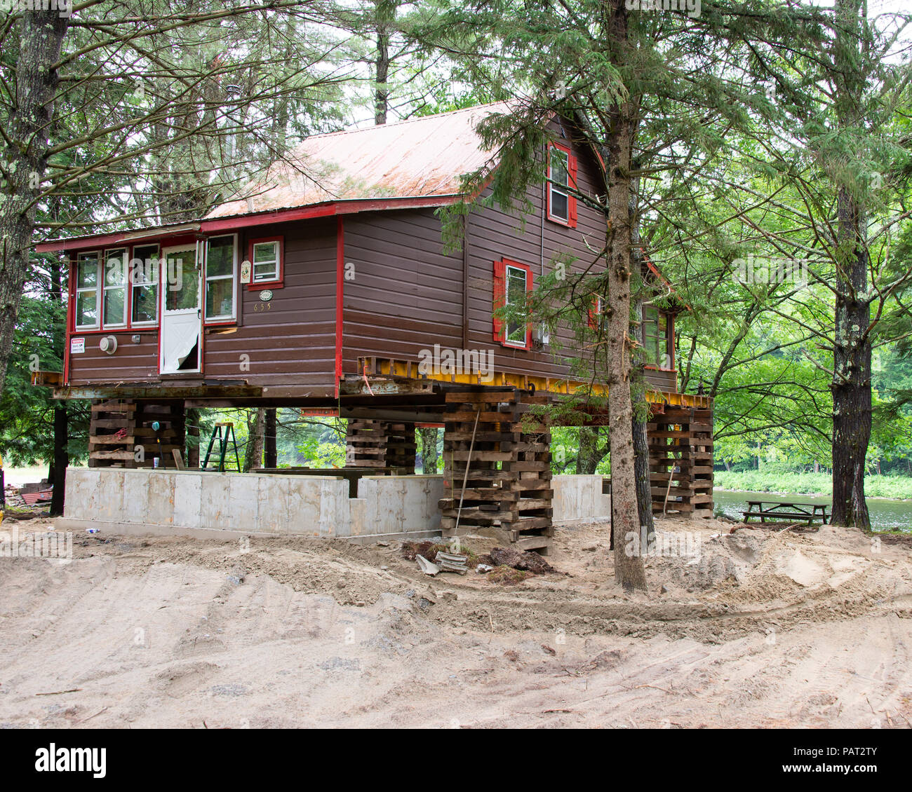 Un marrone telaio in legno casa su un riverfront sollevato per consentire la costruzione di una nuova fondazione in calcestruzzo. Foto Stock