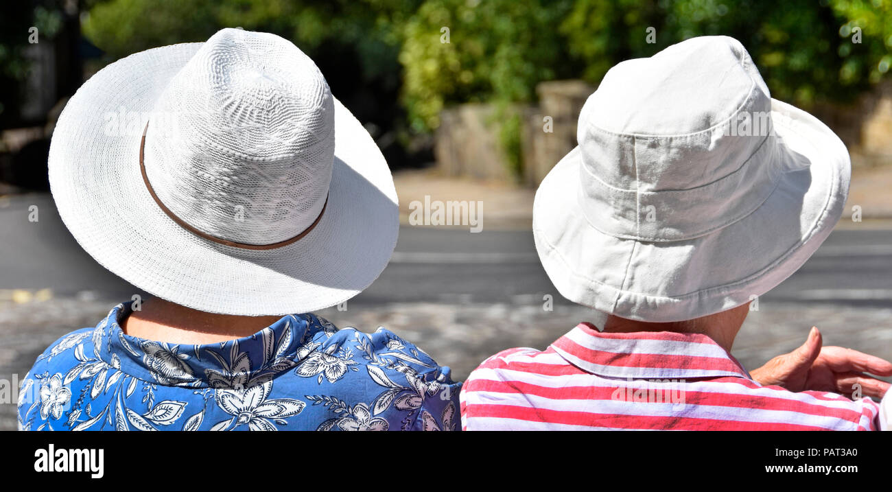 Senior donna matura seduta in attesa presso la fermata su molto caldo 2018 ondata di caldo giorno d'estate indossa cappello bianco nel sole di mezzogiorno Haworth West Yorkshire England Regno Unito Foto Stock