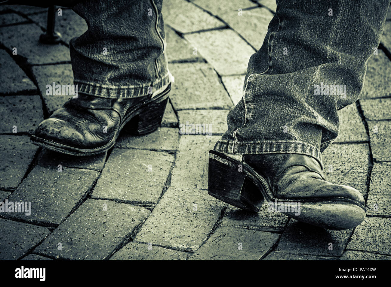 Una chiusura di un uomo in piedi ben indossato stivali da cowboy con grande  tacchi e jeans sulla curva del percorso di mattoni in bianco e nero Foto  stock - Alamy