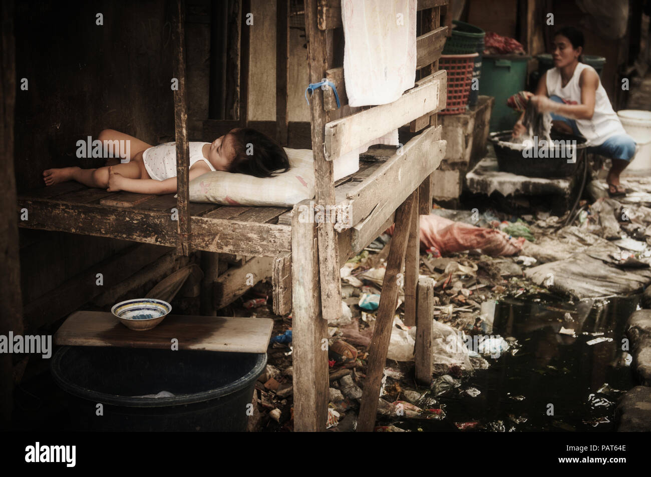 Un bambino dorme sopra un fiume di fognature e spazzatura in Smokey Mountain discarica e le discariche baraccopoli Foto Stock