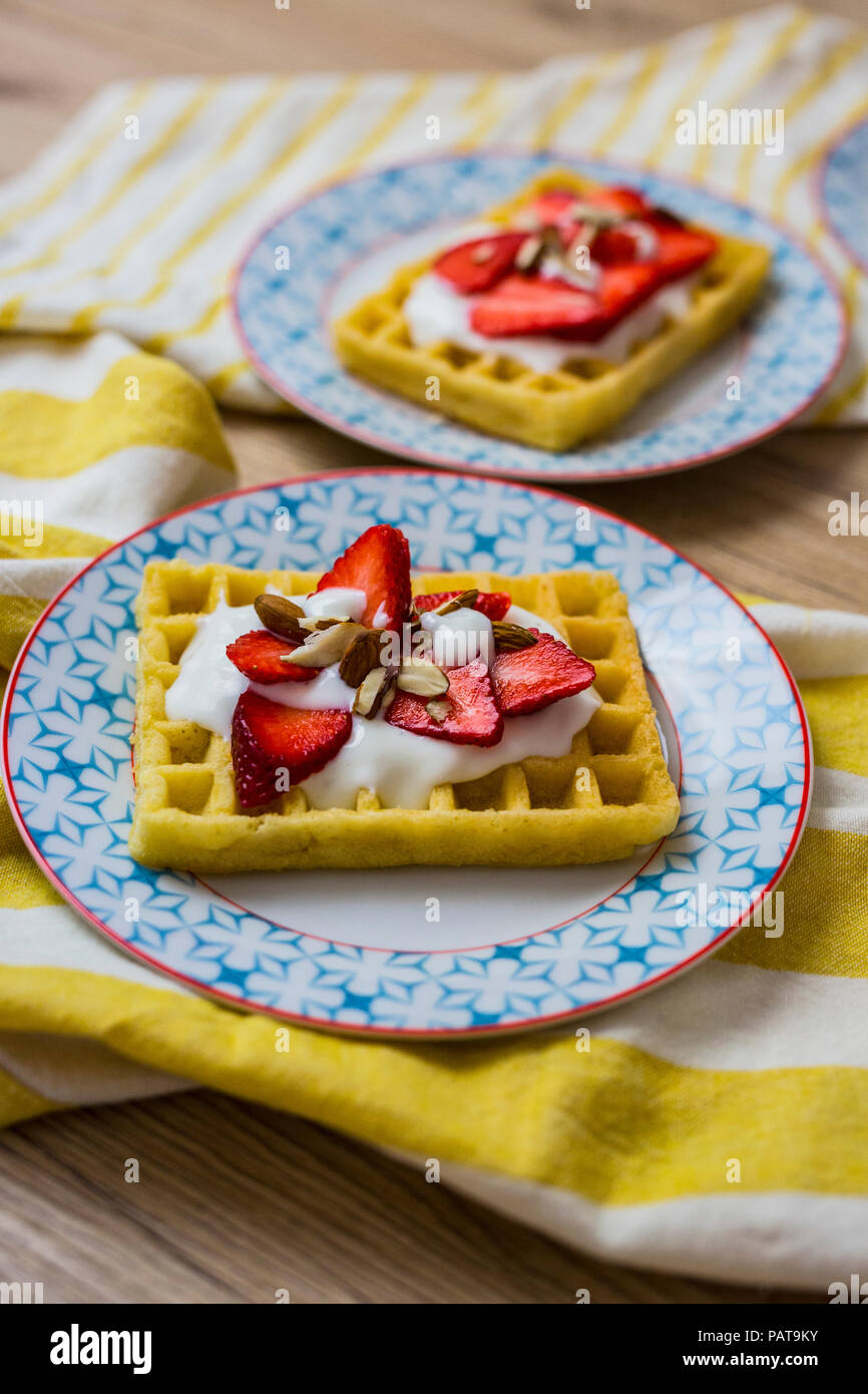 Waffle guarnito con fragole, yogurt greco e mandorle sulla piastra Foto Stock