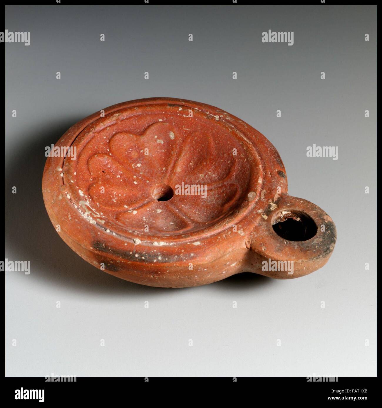 Olio di terracotta con lampada. Cultura: romana, Cnidian. Dimensioni: complessivo: 1 1/8 x 3 3/4 in. (2,9 x 9,5 cm). Data: inizi II secolo D.C.. Loeschcke Tipo 8. Stampo-fatta. Discus: rosette con cinque a forma di cuore petali. Grande, leggermente punta ugello. Entro impressionato base ad anello, debolmente inscritto in lettere greche: ROMANE/SIS, con piccolo cerchio di seguito. Slittare in Alto ma solo in piccole macchie sui lati e la base. Museo: Metropolitan Museum of Art di New York, Stati Uniti d'America. Foto Stock