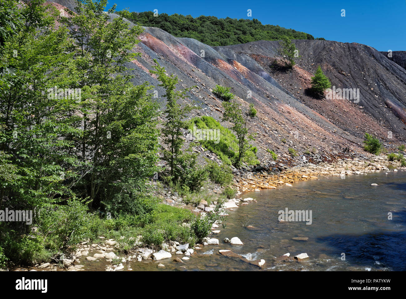 Miniera di carbone rifiuti recupero cumulo accanto a un flusso con rocce di colore arancione che mostra i danni ambientali da inquinamento tossico e acido miniera drenaggio. Foto Stock