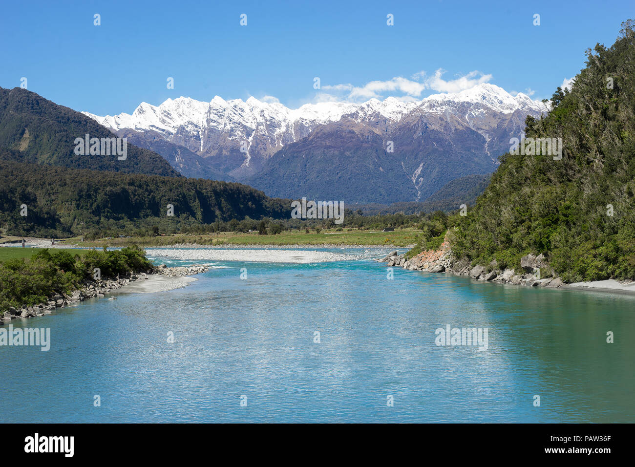 Nuova Zelanda paesaggi, montagne con la neve sulla sommità con turchesi riverfront nella foresta e cielo blu in background Foto Stock