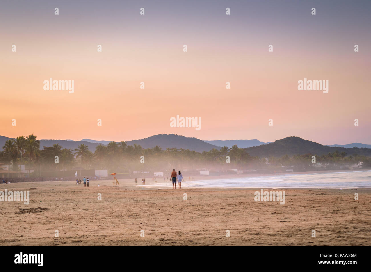 La gente camminare sulla spiaggia al tramonto Foto Stock