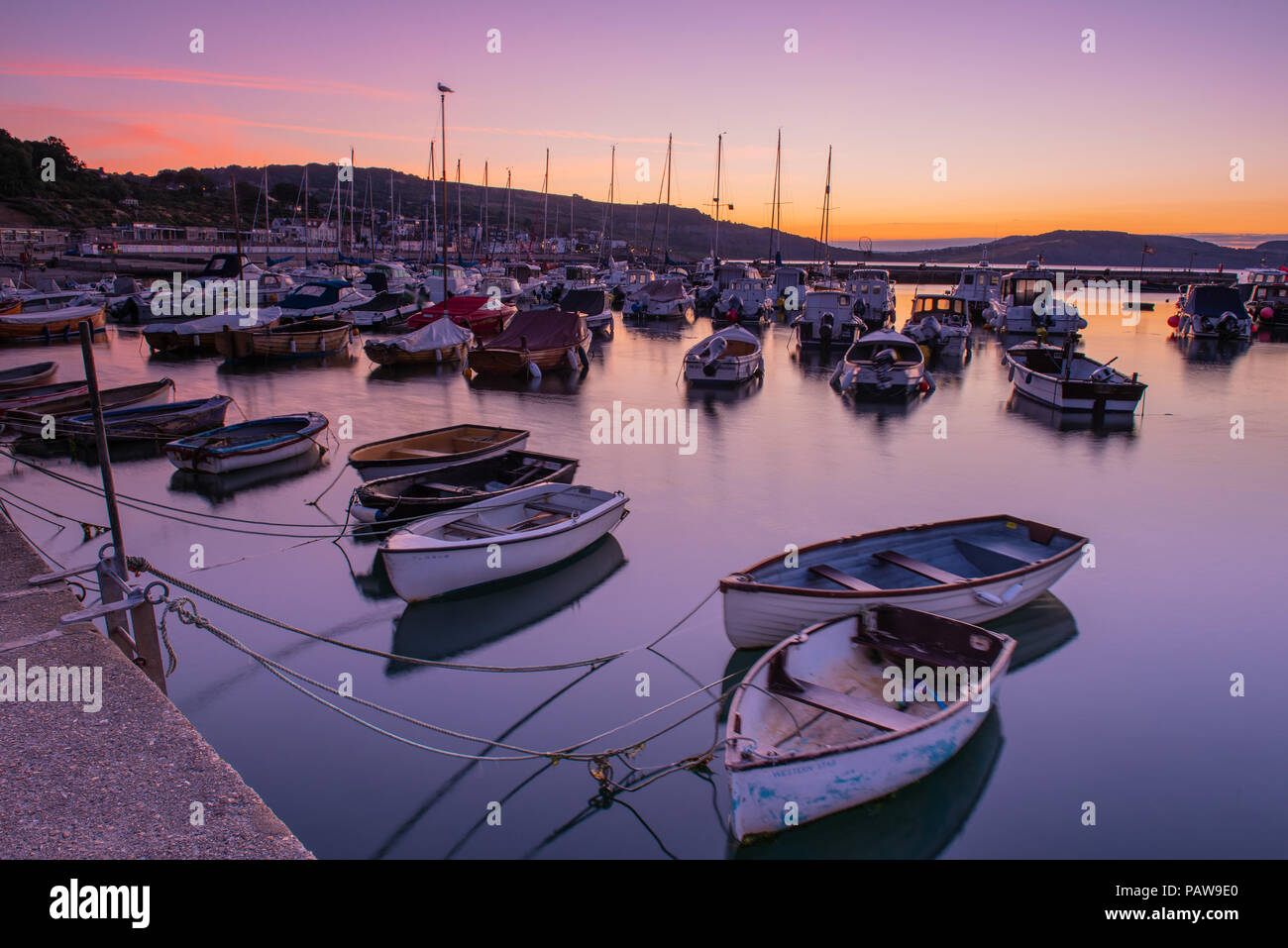 Lyme Regis, Dorset, Regno Unito. Il 25 luglio 2018. Meteo REGNO UNITO: Golden sunrise a Lyme Regis. Le barche nel porto si stagliano contro il bagliore dorato della mattina presto sky su un altro calda e soleggiata giornata nella località costiera comune di Lyme Regis. Credito: Celia McMahon/Alamy Live News. Foto Stock