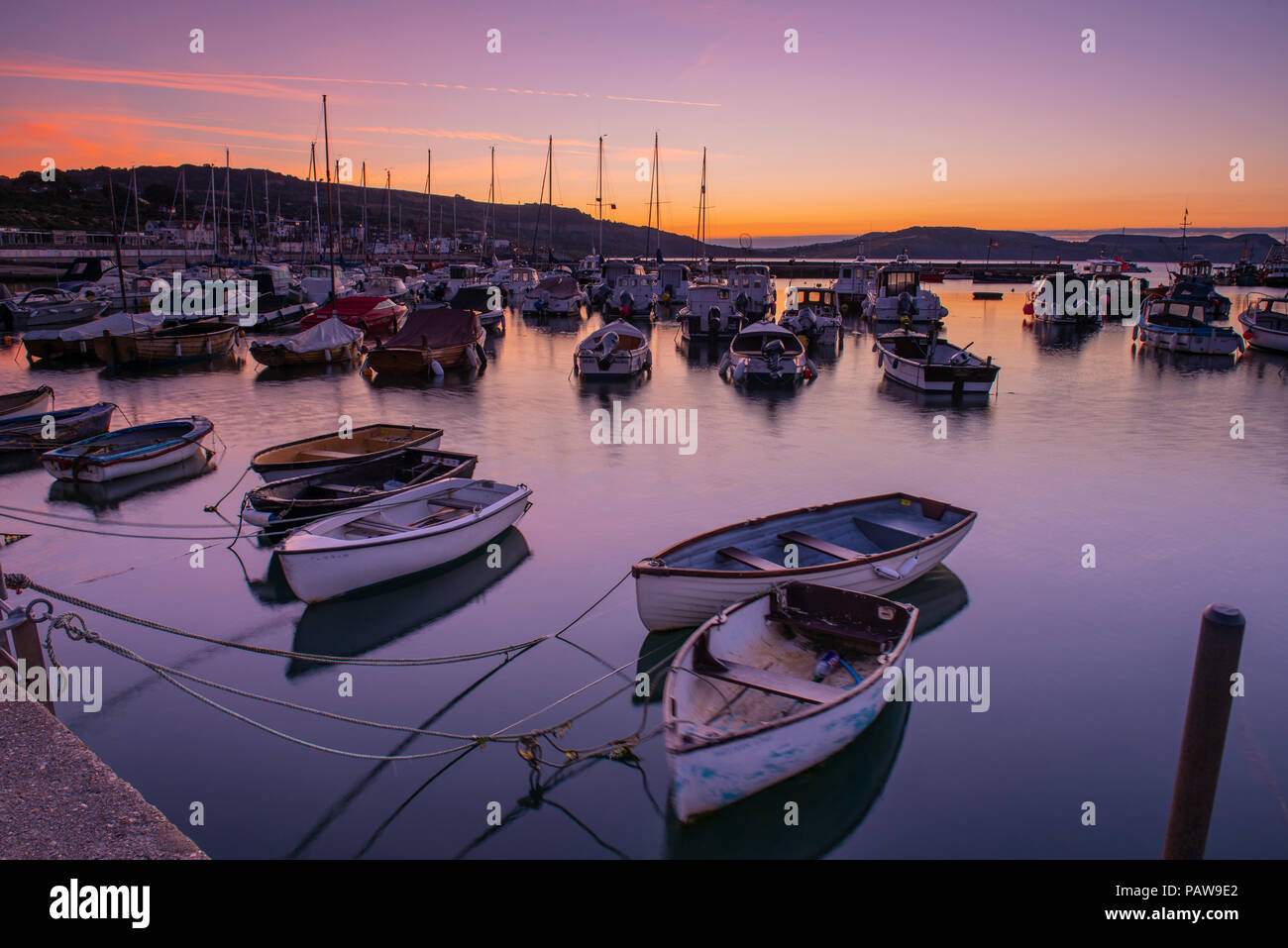 Lyme Regis, Dorset, Regno Unito. Il 25 luglio 2018. Meteo REGNO UNITO: Golden sunrise a Lyme Regis. Le barche nel porto si stagliano contro il bagliore dorato della mattina presto sky su un altro calda e soleggiata giornata nella località costiera comune di Lyme Regis. Credito: Celia McMahon/Alamy Live News. Foto Stock