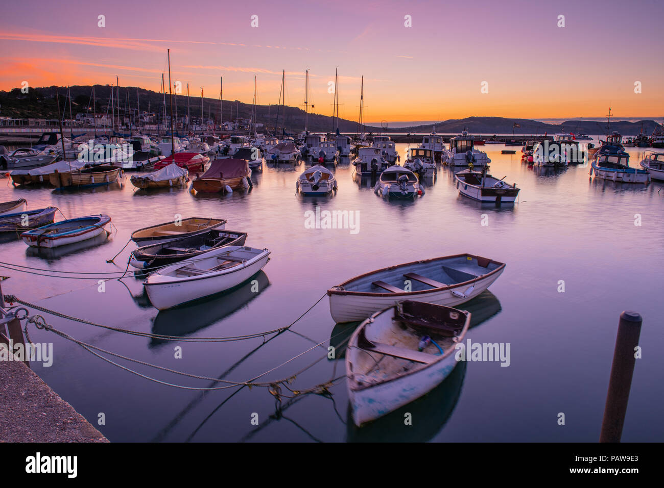 Lyme Regis, Dorset, Regno Unito. Il 25 luglio 2018. Meteo REGNO UNITO: Golden sunrise a Lyme Regis. Le barche nel porto si stagliano contro il bagliore dorato della mattina presto sky su un altro calda e soleggiata giornata nella località costiera comune di Lyme Regis. Credito: Celia McMahon/Alamy Live News. Foto Stock
