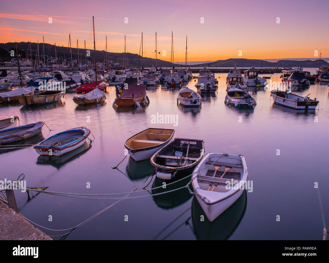 Lyme Regis, Dorset, Regno Unito. Il 25 luglio 2018. Meteo REGNO UNITO: Golden sunrise a Lyme Regis. Le barche nel porto si stagliano contro il bagliore dorato della mattina presto sky su un altro calda e soleggiata giornata nella località costiera comune di Lyme Regis. Credito: Celia McMahon/Alamy Live News. Foto Stock