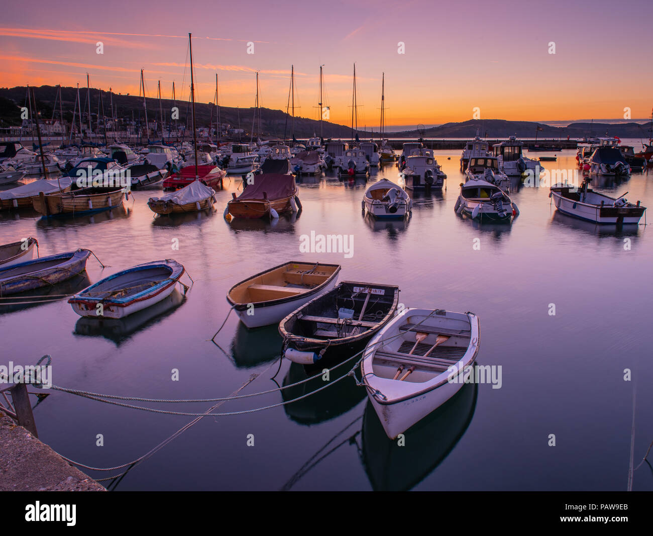 Lyme Regis, Dorset, Regno Unito. Il 25 luglio 2018. Meteo REGNO UNITO: Golden sunrise a Lyme Regis. Le barche nel porto si stagliano contro il bagliore dorato della mattina presto sky su un altro calda e soleggiata giornata nella località costiera comune di Lyme Regis. Credito: Celia McMahon/Alamy Live News. Foto Stock
