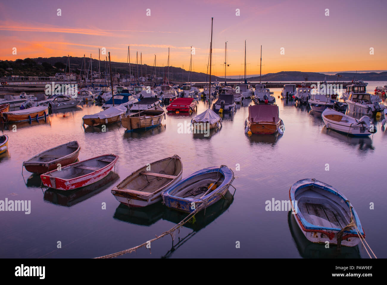 Lyme Regis, Dorset, Regno Unito. Il 25 luglio 2018. Meteo REGNO UNITO: Golden sunrise a Lyme Regis. Le barche nel porto si stagliano contro il bagliore dorato della mattina presto sky su un altro calda e soleggiata giornata nella località costiera comune di Lyme Regis. Credito: Celia McMahon/Alamy Live News. Foto Stock