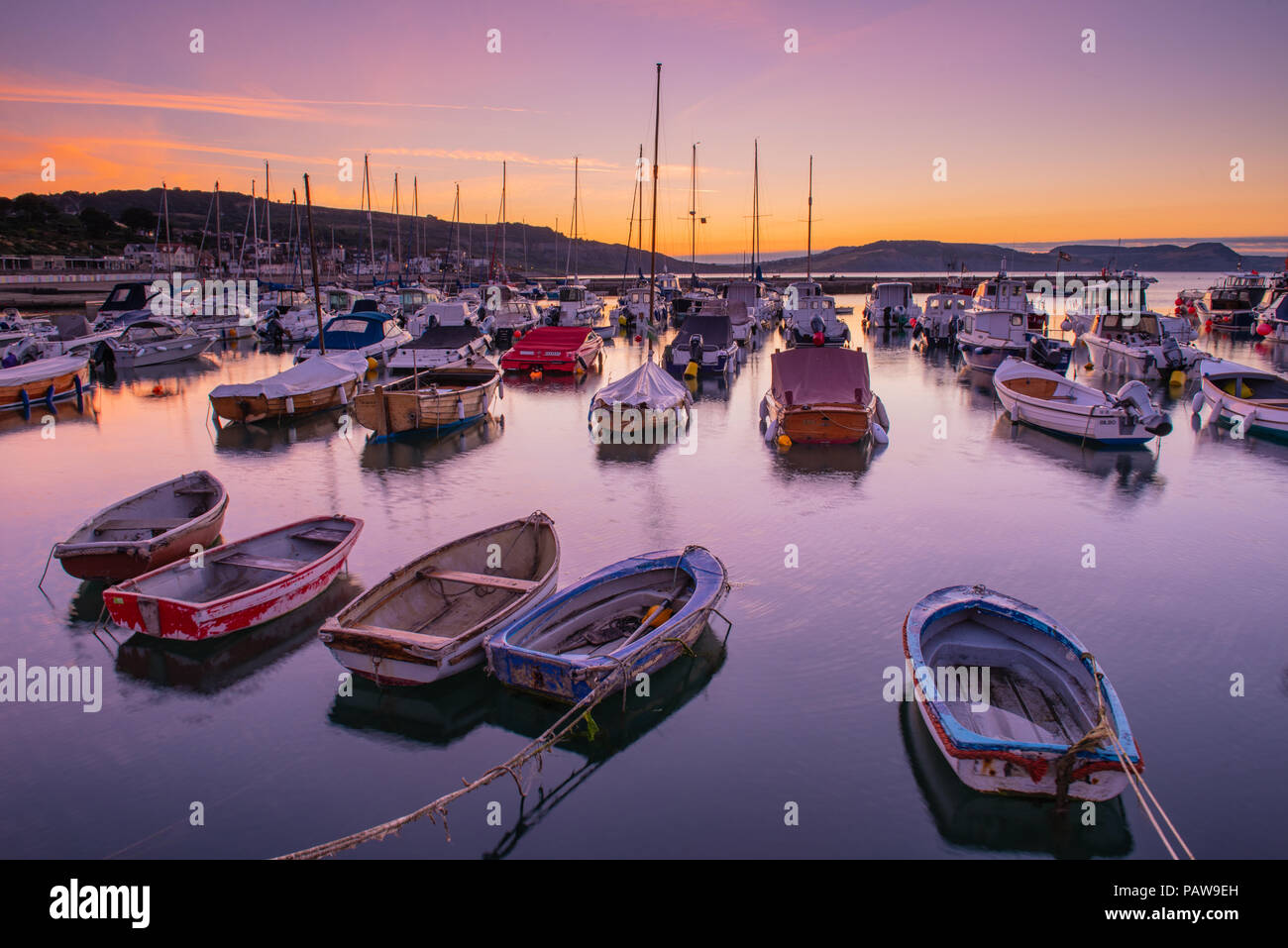 Lyme Regis, Dorset, Regno Unito. Il 25 luglio 2018. Meteo REGNO UNITO: Golden sunrise a Lyme Regis. Le barche nel porto si stagliano contro il bagliore dorato della mattina presto sky su un altro calda e soleggiata giornata nella località costiera comune di Lyme Regis. Credito: Celia McMahon/Alamy Live News. Foto Stock