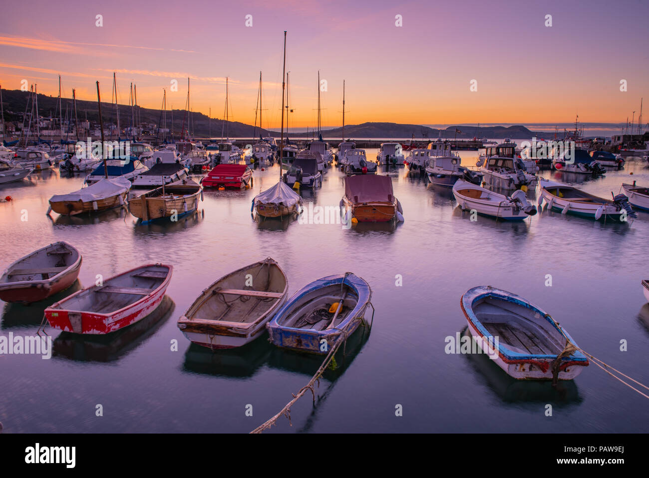 Lyme Regis, Dorset, Regno Unito. Il 25 luglio 2018. Meteo REGNO UNITO: Golden sunrise a Lyme Regis. Le barche nel porto si stagliano contro il bagliore dorato della mattina presto sky su un altro calda e soleggiata giornata nella località costiera comune di Lyme Regis. Credito: Celia McMahon/Alamy Live News. Foto Stock