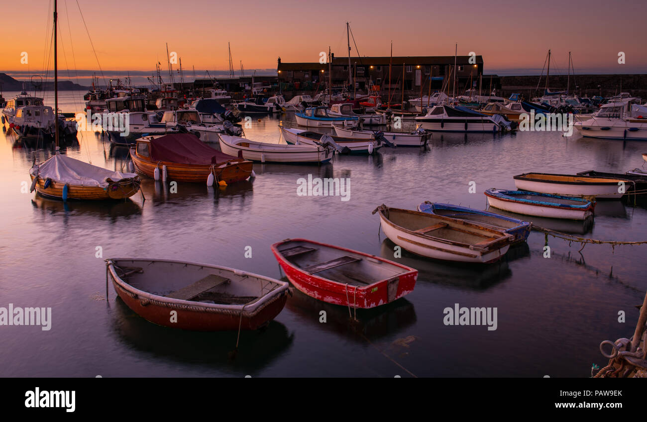 Lyme Regis, Dorset, Regno Unito. Il 25 luglio 2018. Meteo REGNO UNITO: Golden sunrise a Lyme Regis. Le barche nel porto si stagliano contro il bagliore dorato della mattina presto sky su un altro calda e soleggiata giornata nella località costiera comune di Lyme Regis. Credito: Celia McMahon/Alamy Live News. Foto Stock