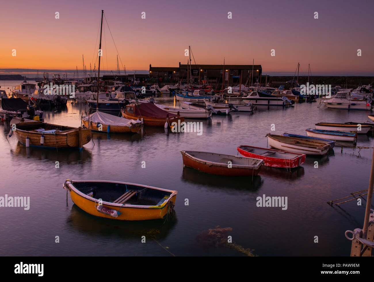 Lyme Regis, Dorset, Regno Unito. Il 25 luglio 2018. Meteo REGNO UNITO: Golden sunrise a Lyme Regis. Le barche nel porto si stagliano contro il bagliore dorato della mattina presto sky su un altro calda e soleggiata giornata nella località costiera comune di Lyme Regis. Credito: Celia McMahon/Alamy Live News. Foto Stock