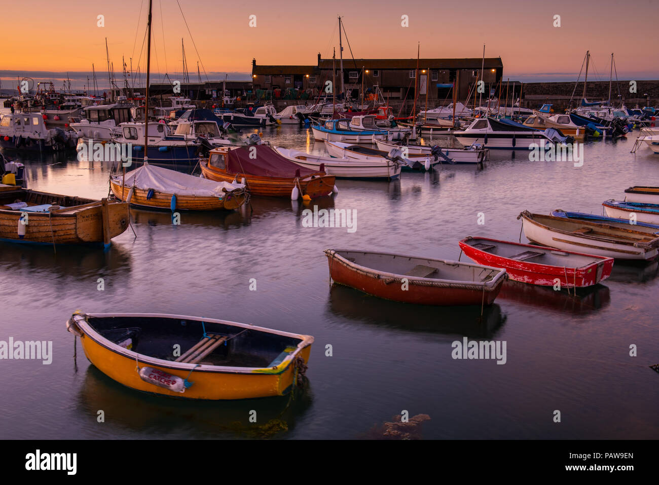 Lyme Regis, Dorset, Regno Unito. Il 25 luglio 2018. Meteo REGNO UNITO: Golden sunrise a Lyme Regis. Le barche nel porto si stagliano contro il bagliore dorato della mattina presto sky su un altro calda e soleggiata giornata nella località costiera comune di Lyme Regis. Credito: Celia McMahon/Alamy Live News. Foto Stock