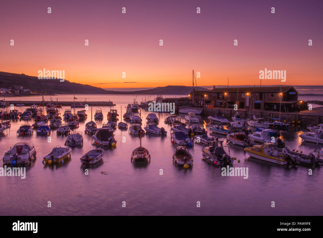 Lyme Regis, Dorset, Regno Unito. Il 25 luglio 2018. Meteo REGNO UNITO: Golden sunrise a Lyme Regis. Le barche nel porto si stagliano contro il bagliore dorato della mattina presto sky su un altro calda e soleggiata giornata nella località costiera comune di Lyme Regis. Credito: Celia McMahon/Alamy Live News. Foto Stock