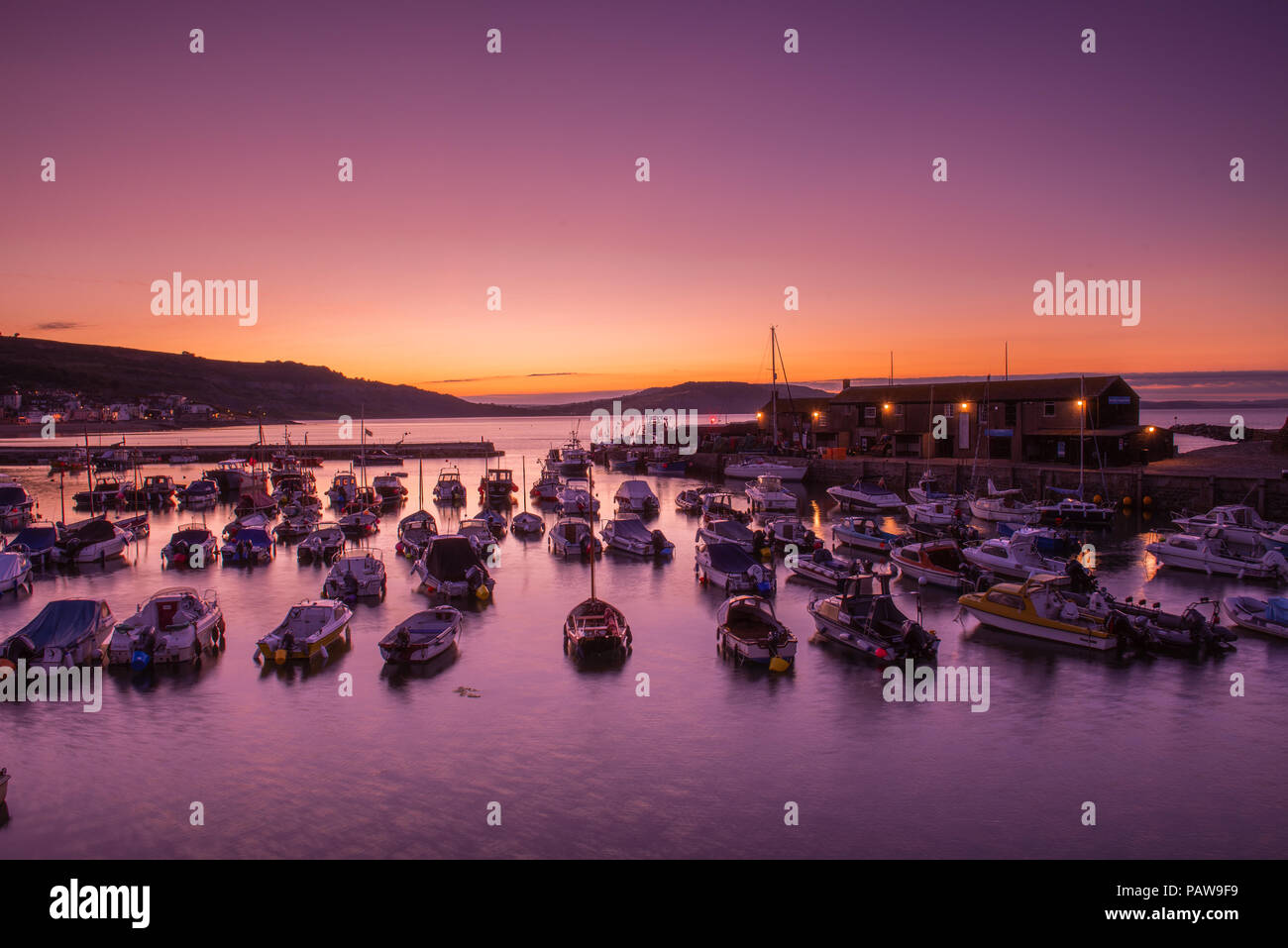 Lyme Regis, Dorset, Regno Unito. Il 25 luglio 2018. Meteo REGNO UNITO: Golden sunrise a Lyme Regis. Le barche nel porto si stagliano contro il bagliore dorato della mattina presto sky su un altro calda e soleggiata giornata nella località costiera comune di Lyme Regis. Credito: Celia McMahon/Alamy Live News. Foto Stock