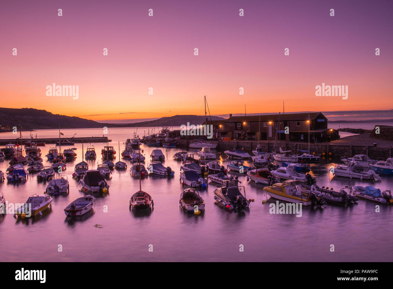 Lyme Regis, Dorset, Regno Unito. Il 25 luglio 2018. Meteo REGNO UNITO: Golden sunrise a Lyme Regis. Le barche nel porto si stagliano contro il bagliore dorato della mattina presto sky su un altro calda e soleggiata giornata nella località costiera comune di Lyme Regis. Credito: Celia McMahon/Alamy Live News. Foto Stock